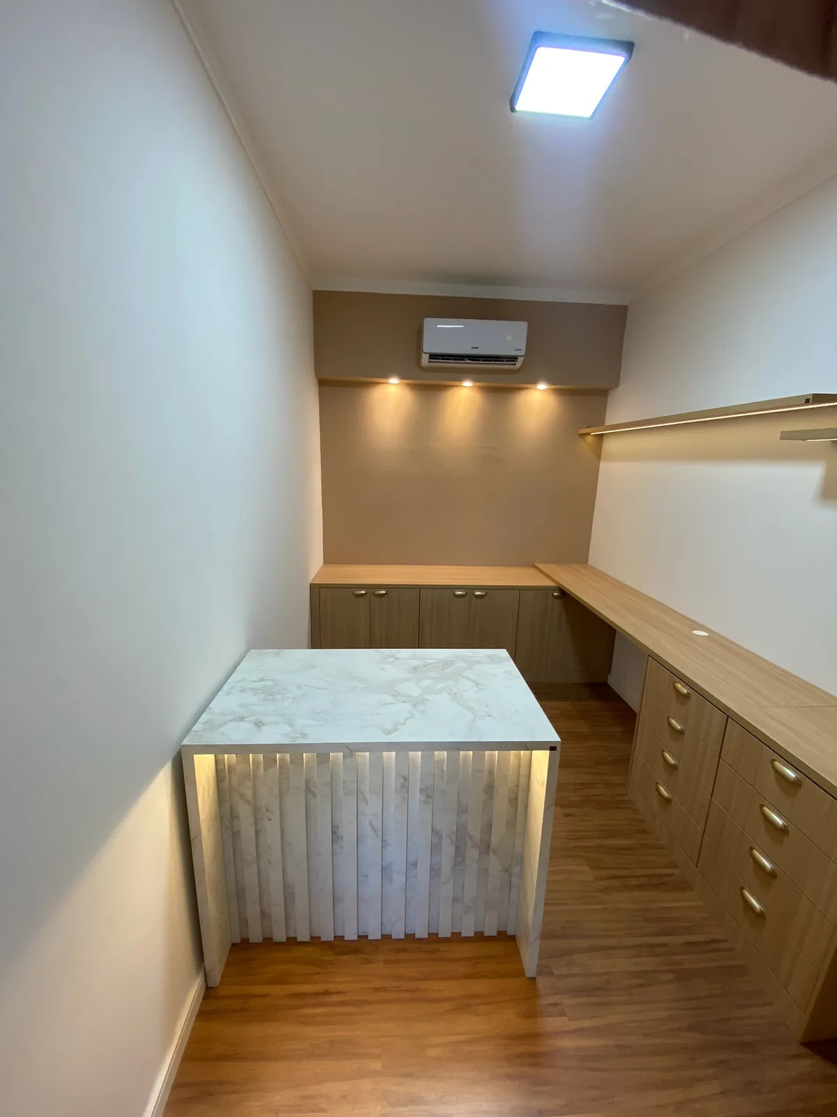 Closet planejado em madeira com nichos, gavetas e iluminação no acabamento.