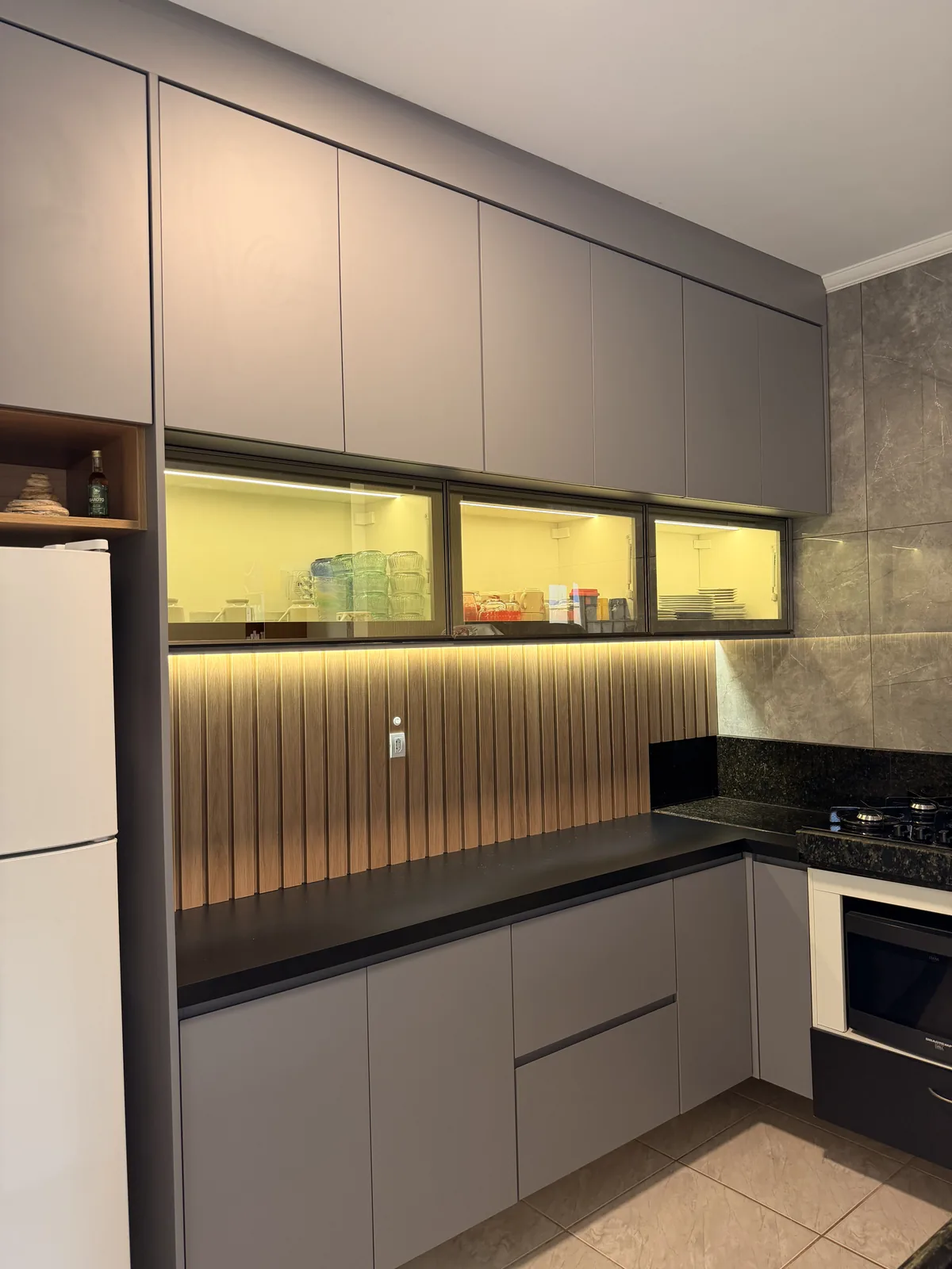 Cozinha planejada com painel ripado, armários escuros e bancada iluminada.